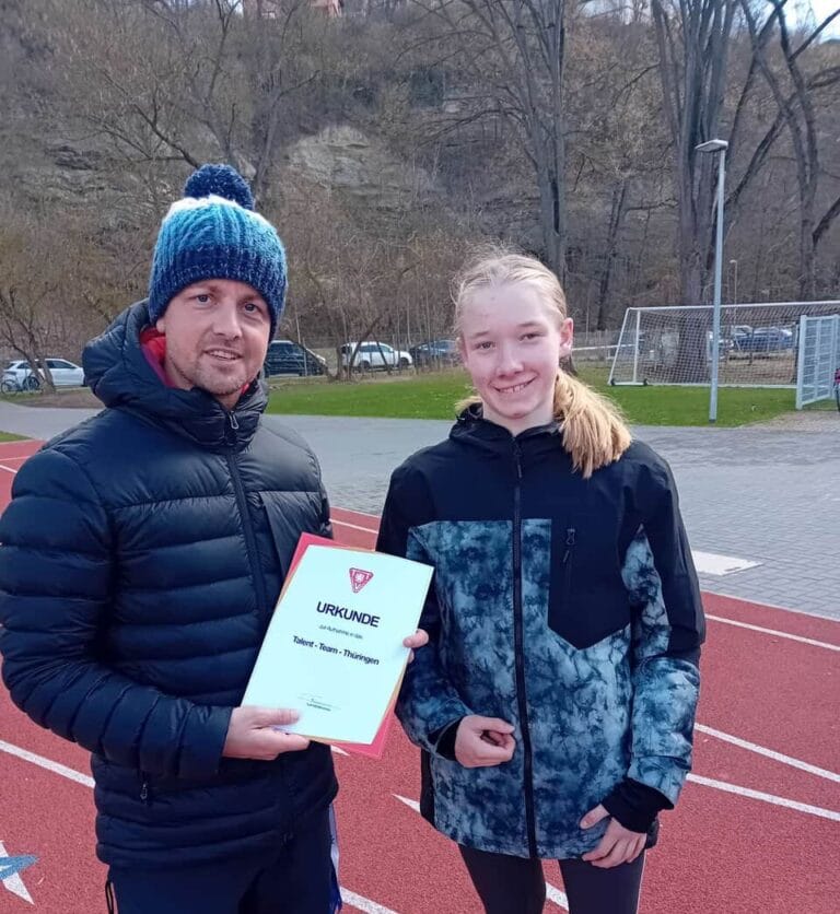 Trainer übergibt Urkunde an Athletin