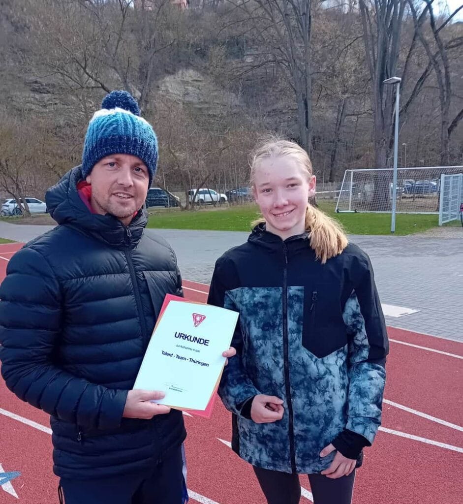 Trainer übergibt Urkunde an Athletin